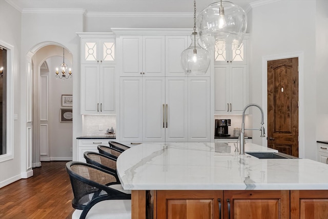 kitchen featuring light stone counters, a kitchen island with sink, sink, pendant lighting, and white cabinetry