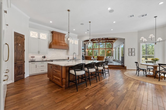 kitchen featuring white cabinets, light stone countertops, premium range hood, and a kitchen island with sink