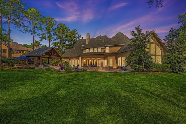 back house at dusk featuring a patio and a lawn