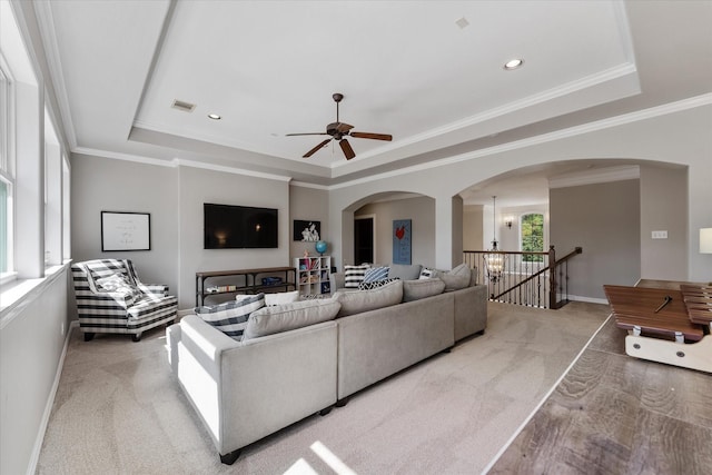 carpeted living room featuring ceiling fan with notable chandelier, a raised ceiling, and ornamental molding