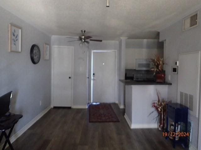 living room with a textured ceiling, ceiling fan, and dark hardwood / wood-style floors