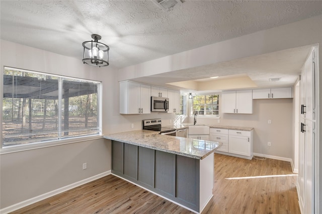 kitchen featuring kitchen peninsula, stainless steel appliances, pendant lighting, light hardwood / wood-style floors, and white cabinetry