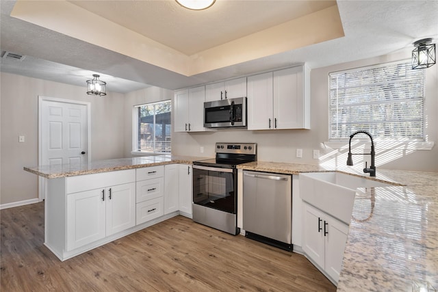 kitchen with white cabinets, light hardwood / wood-style floors, kitchen peninsula, and stainless steel appliances