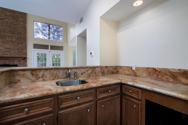 kitchen featuring light stone countertops, french doors, dark brown cabinets, a large fireplace, and sink