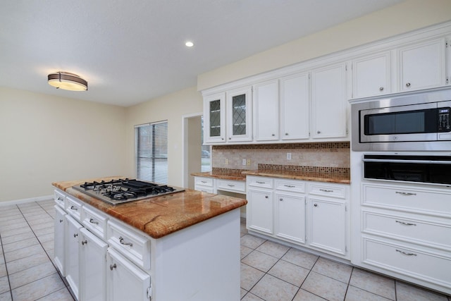 kitchen with a center island, light tile patterned floors, tasteful backsplash, white cabinetry, and stainless steel appliances