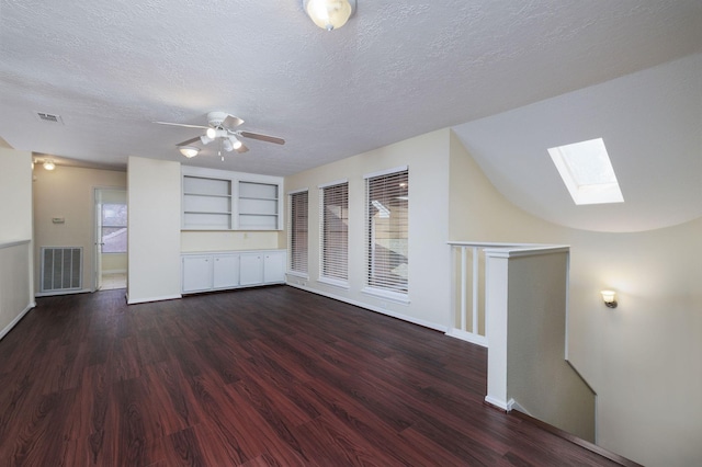 interior space with lofted ceiling with skylight, ceiling fan, dark wood-type flooring, and a textured ceiling