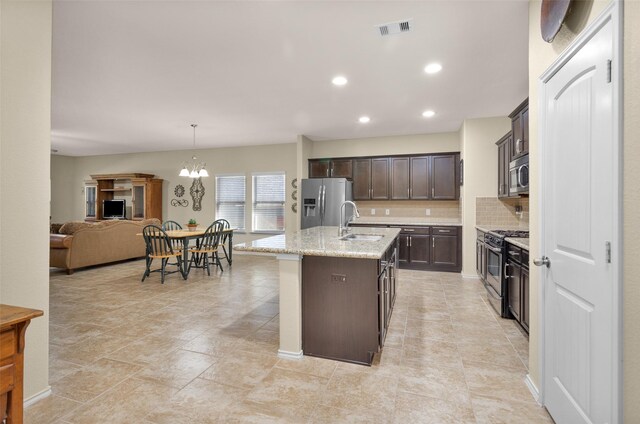 kitchen featuring light stone countertops, dark brown cabinets, stainless steel appliances, a kitchen island with sink, and sink