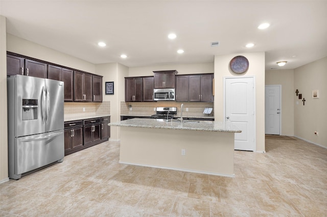 kitchen featuring sink, light stone countertops, an island with sink, dark brown cabinetry, and stainless steel appliances