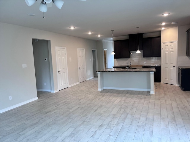 kitchen with sink, decorative backsplash, ceiling fan, a center island with sink, and light wood-type flooring