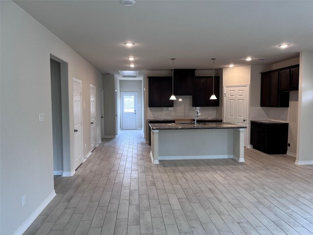 kitchen with a kitchen island with sink, backsplash, sink, and light wood-type flooring