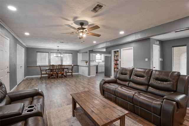 living room with ceiling fan with notable chandelier, dark hardwood / wood-style flooring, a textured ceiling, and ornamental molding