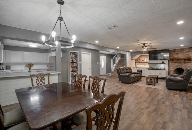 dining space with a fireplace, ceiling fan with notable chandelier, a textured ceiling, and hardwood / wood-style flooring