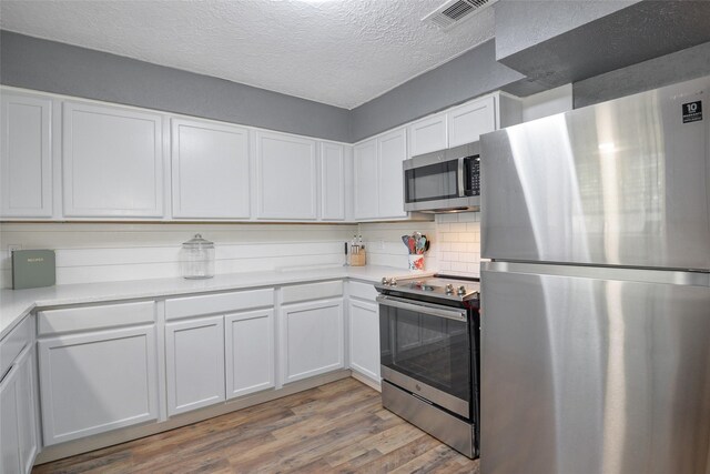 kitchen featuring stainless steel appliances, backsplash, light hardwood / wood-style floors, a textured ceiling, and white cabinets