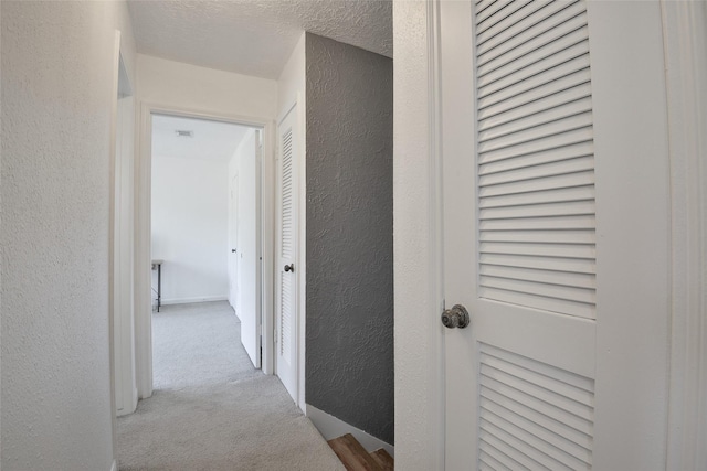 hall with light carpet and a textured ceiling