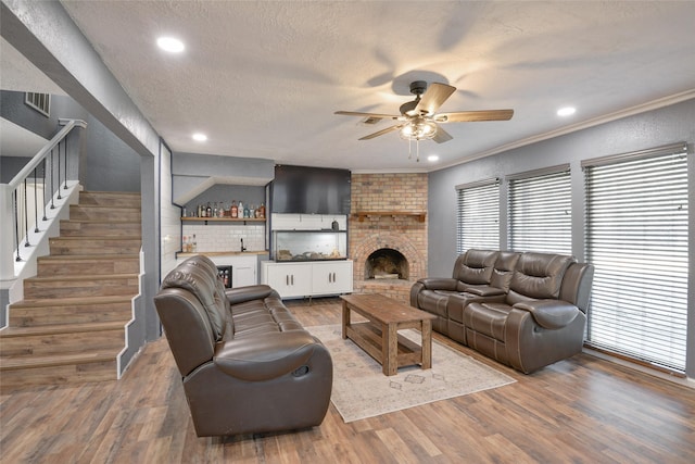 living room with hardwood / wood-style floors, a textured ceiling, a brick fireplace, and ornamental molding