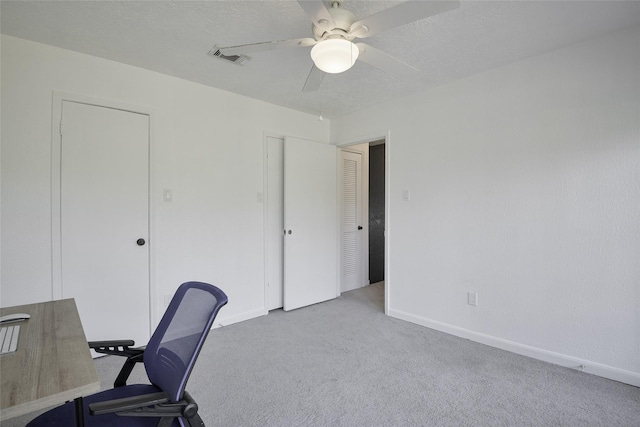 unfurnished office featuring a textured ceiling, light colored carpet, and ceiling fan