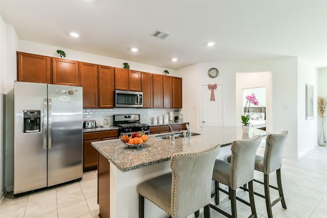 kitchen with a breakfast bar, sink, light tile patterned floors, an island with sink, and stainless steel appliances