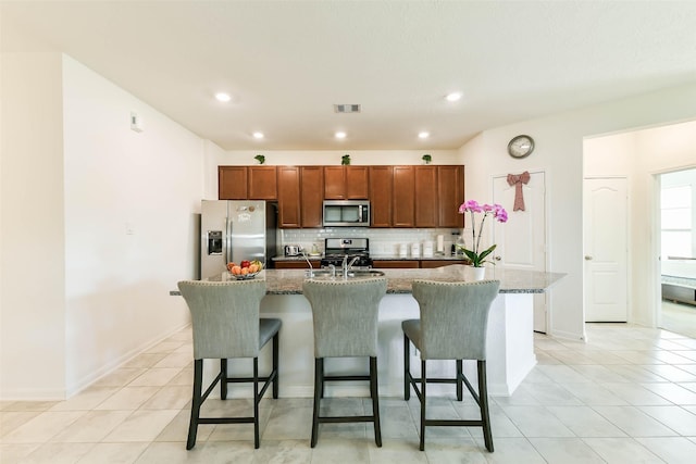 kitchen with dark stone counters, stainless steel appliances, an island with sink, a breakfast bar area, and light tile patterned flooring