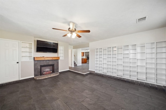 unfurnished living room featuring ceiling fan, built in shelves, a textured ceiling, and a tiled fireplace