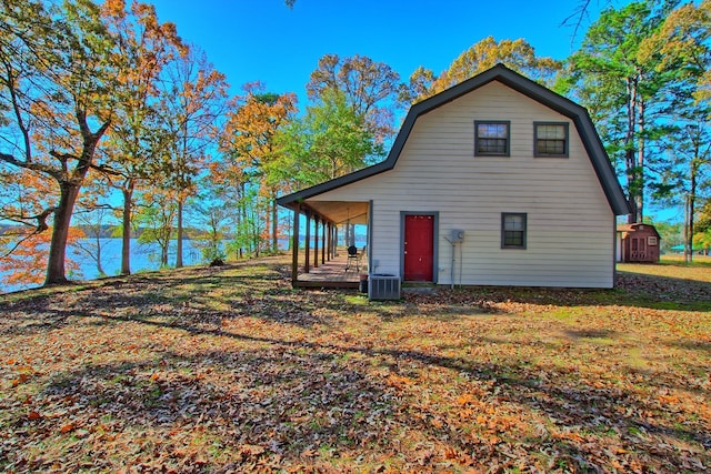 rear view of property featuring a lawn, a storage unit, covered porch, and central air condition unit