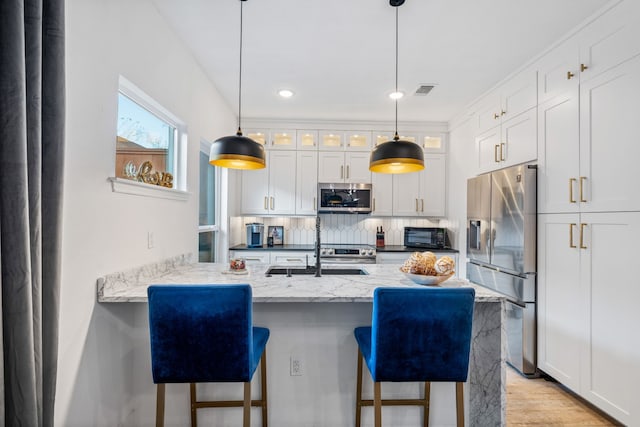 kitchen with appliances with stainless steel finishes, light stone counters, sink, white cabinets, and a breakfast bar area