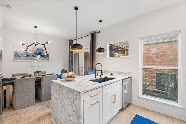 kitchen with sink, hanging light fixtures, stainless steel dishwasher, light stone counters, and white cabinetry