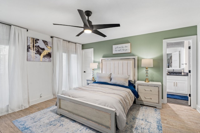 bedroom featuring light wood-type flooring, ensuite bathroom, ceiling fan, and sink