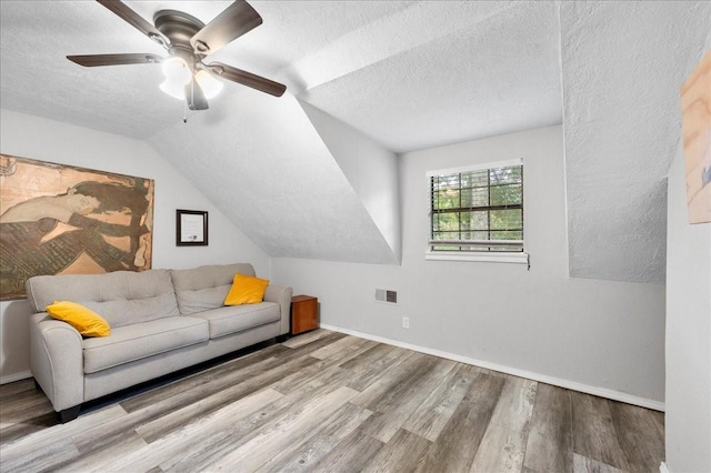 living room with vaulted ceiling, ceiling fan, a textured ceiling, and light wood-type flooring