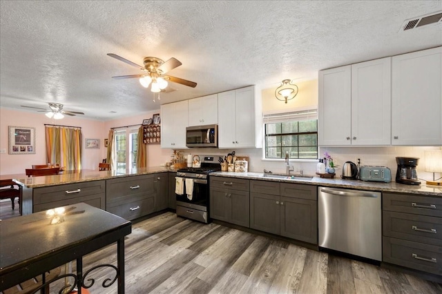 kitchen featuring light wood-type flooring, stainless steel appliances, sink, stone counters, and white cabinets