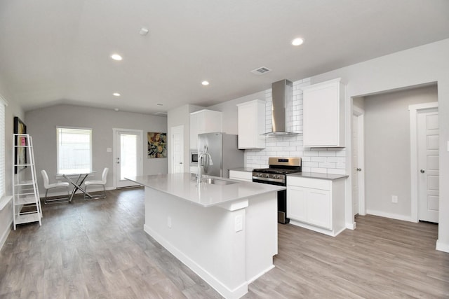 kitchen with a kitchen island with sink, white cabinets, wall chimney range hood, decorative backsplash, and stainless steel appliances