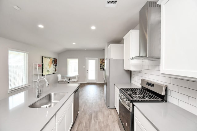 kitchen featuring white cabinetry, sink, wall chimney exhaust hood, lofted ceiling, and appliances with stainless steel finishes