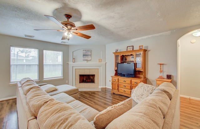 living room featuring a textured ceiling, ceiling fan, wood-type flooring, and a fireplace