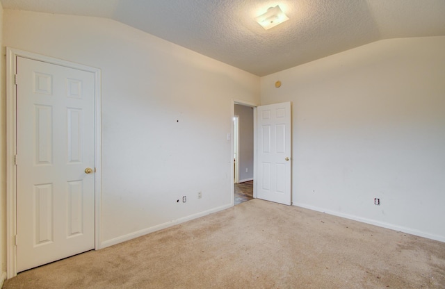 empty room with light colored carpet, a textured ceiling, and vaulted ceiling