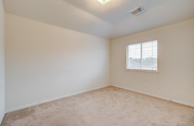 spare room with vaulted ceiling, light carpet, and a textured ceiling