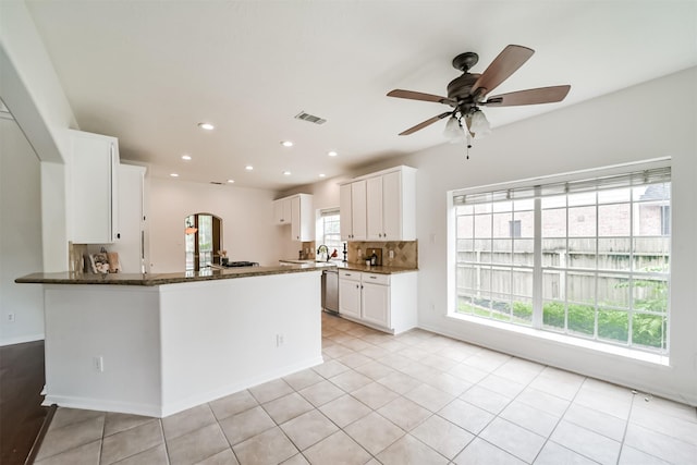 kitchen featuring ceiling fan, stainless steel dishwasher, kitchen peninsula, dark stone counters, and white cabinets