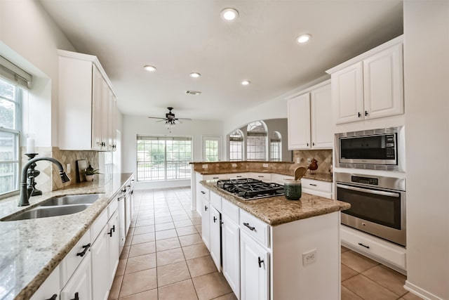 kitchen featuring light stone countertops, appliances with stainless steel finishes, ceiling fan, sink, and a center island