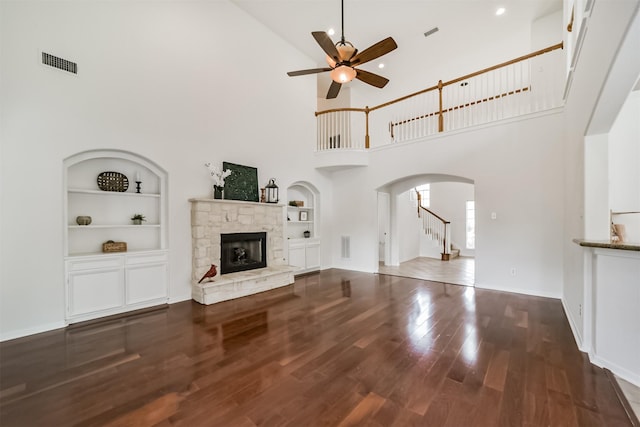 unfurnished living room with a high ceiling, built in shelves, ceiling fan, a fireplace, and wood-type flooring