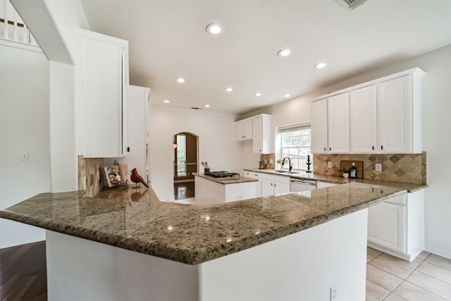 kitchen featuring white cabinets, stainless steel dishwasher, dark stone countertops, light tile patterned floors, and kitchen peninsula