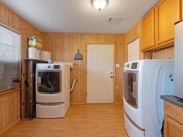 washroom with cabinets, a textured ceiling, wooden walls, separate washer and dryer, and light hardwood / wood-style floors