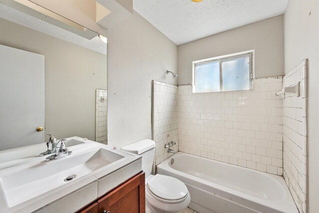 full bathroom featuring a textured ceiling, vanity, toilet, and tiled shower / bath