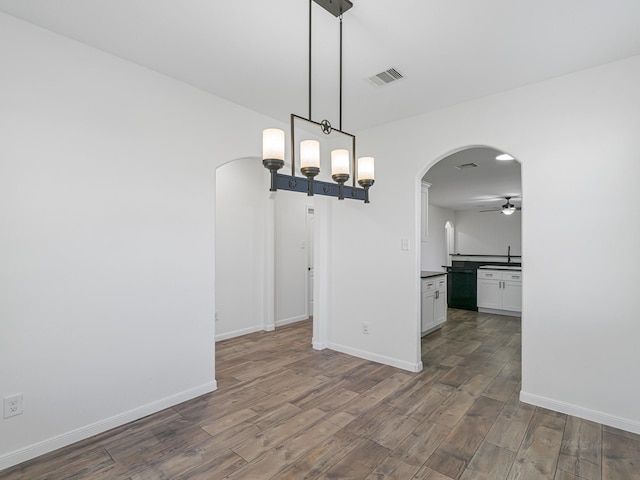 unfurnished dining area featuring ceiling fan with notable chandelier and sink