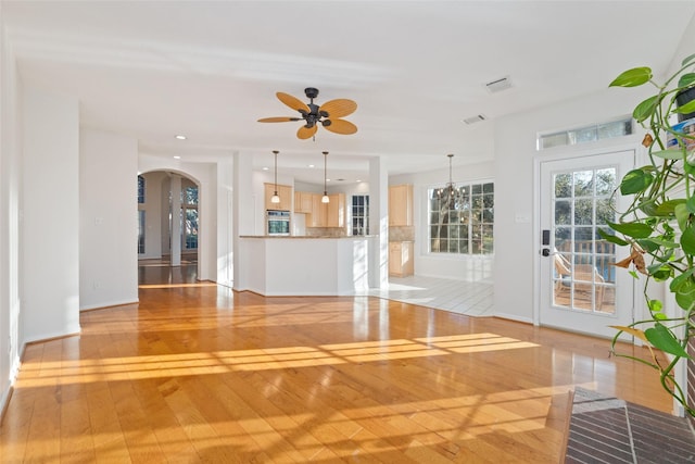 unfurnished living room featuring ceiling fan with notable chandelier and light wood-type flooring