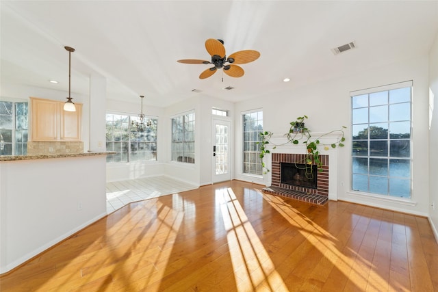 unfurnished living room with ceiling fan with notable chandelier, light hardwood / wood-style floors, and a brick fireplace