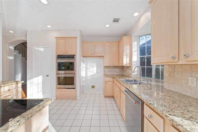 kitchen with light stone countertops, sink, stainless steel appliances, tasteful backsplash, and light brown cabinetry