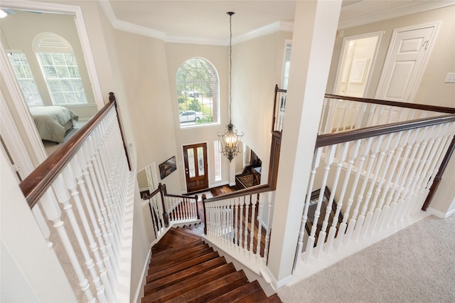 stairs featuring ornamental molding, a wealth of natural light, and an inviting chandelier