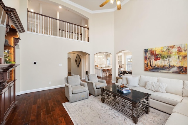 living room featuring ornamental molding, dark wood-type flooring, ceiling fan, and a towering ceiling