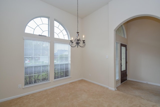 carpeted empty room with a high ceiling and a notable chandelier