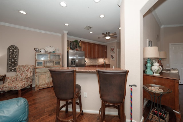 kitchen featuring dark wood-type flooring, crown molding, kitchen peninsula, decorative backsplash, and stainless steel fridge with ice dispenser