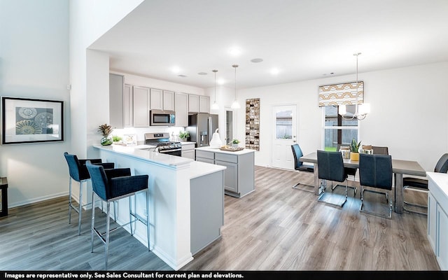 kitchen with kitchen peninsula, appliances with stainless steel finishes, a breakfast bar, decorative light fixtures, and gray cabinets