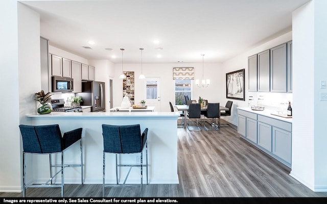 kitchen featuring a kitchen breakfast bar, kitchen peninsula, pendant lighting, gray cabinets, and appliances with stainless steel finishes